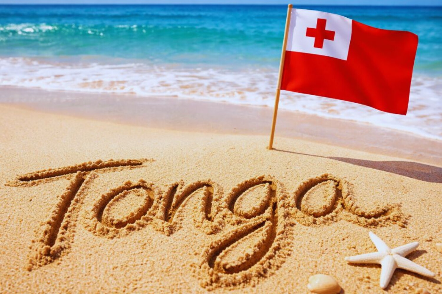 Tonga written in sand with a Tongan flag sticking out of the sand.